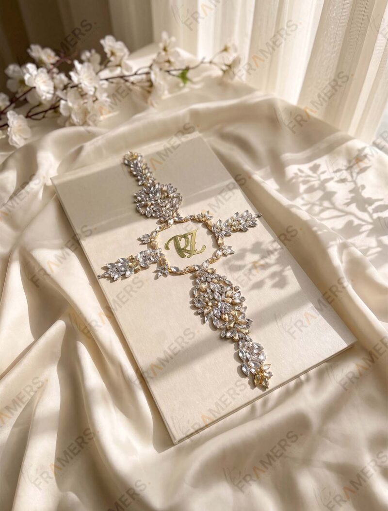 Close-up of an ivory Nikkah booklet cover with a clear crystal cross and gold initials