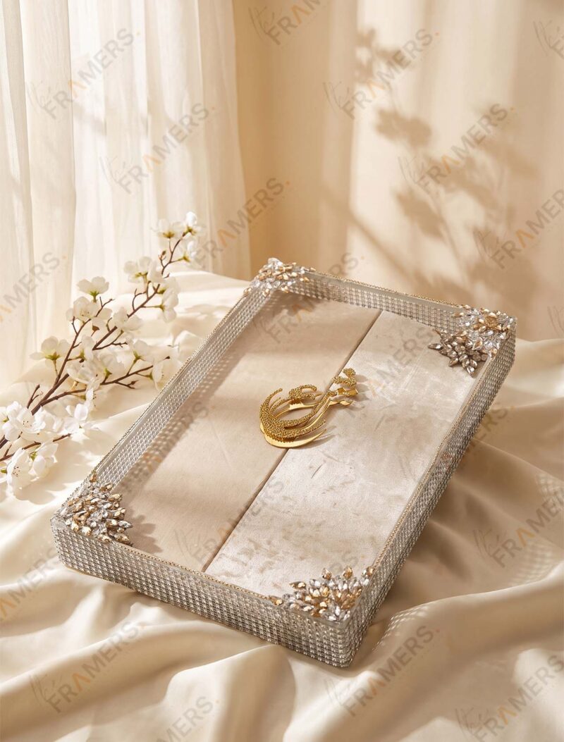 Cream velvet Nikkah booklet resting in a clear crystal tray with a gold calligraphy piece