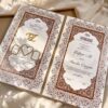 Soft gold Nikkah booklet opened to show initials, rings, names and a copper floral border